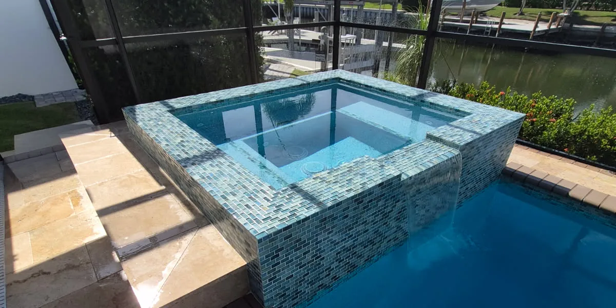 After: the same raised spa clad in blue and green glass mosaic across the rim, the outer face and a new spillway, spilling into a pool with a deep blue interior finish
