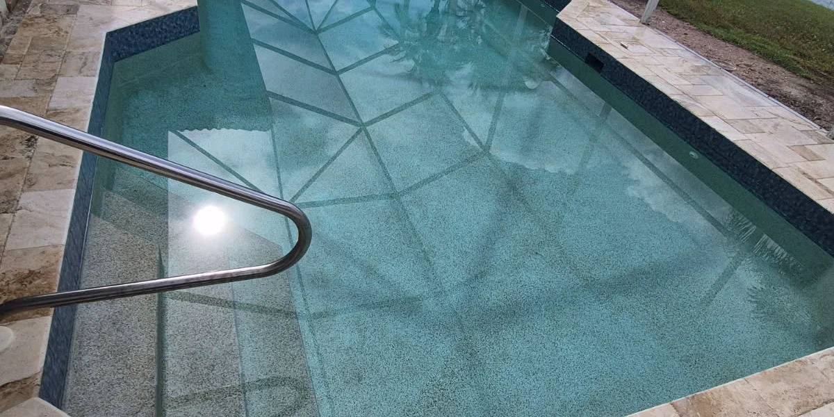 After: French-pattern travertine deck and coping around a lakefront screened pool, with dark teal glass mosaic waterline tile