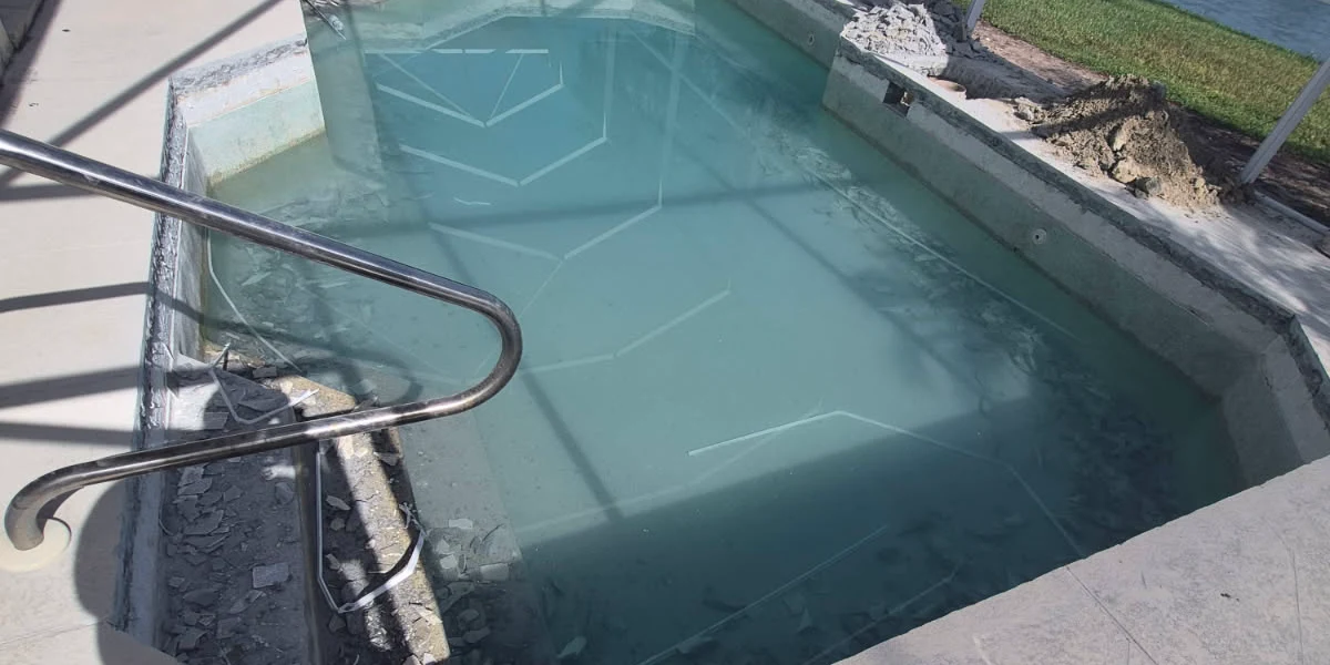 Before: the same lakefront pool mid-demolition, coping and waterline tile chipped off, broken tile in the water and a plain concrete deck